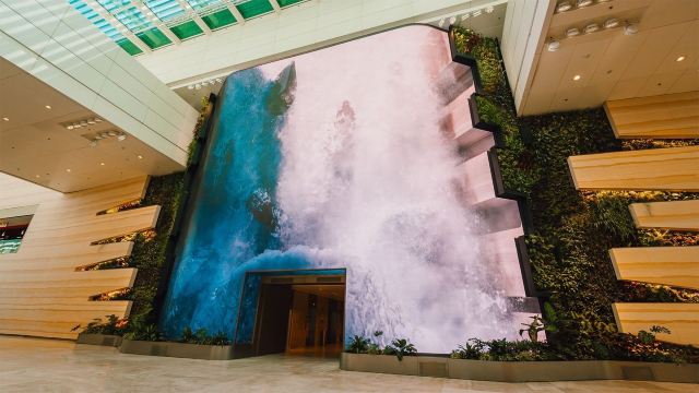 Large digital waterfall display surrounded by greenery inside Changi Airport