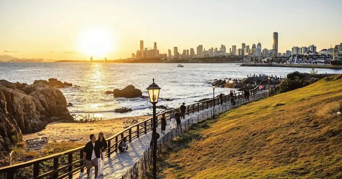 Parque Xiaomaidao en Qingdao con paseo marítimo y vistas al skyline de la ciudad al atardecer.