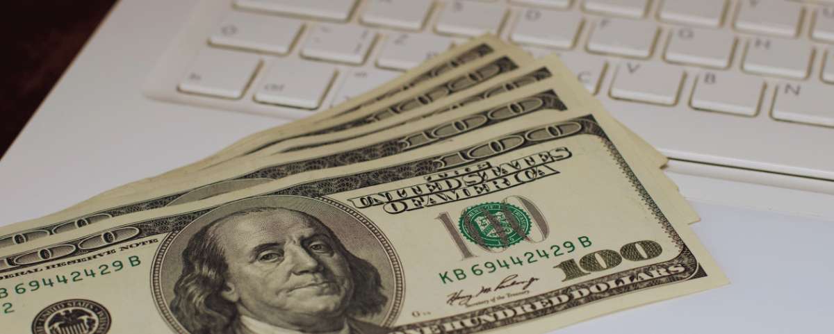 One hundred dollar bills spread out next to a white keyboard