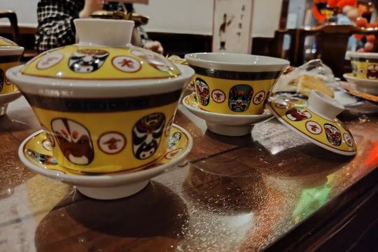 Yellow Chinese gaiwan tea set decorated with traditional opera masks at Lao She Teahouse
