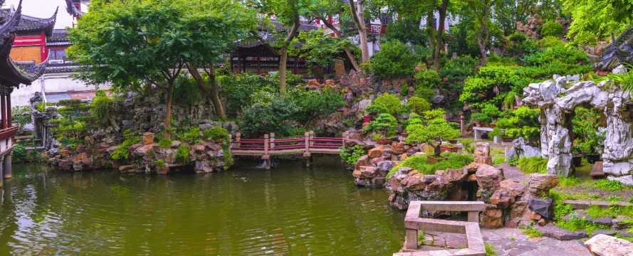 Paisaje del Jardín Yuyuan con estanque, puente de piedra y vegetación en un parque histórico de Shanghái.
