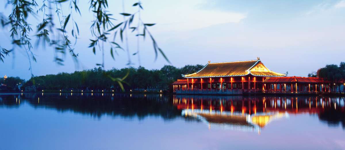 Pavillon chinois traditionnel illuminé au bord d'un lac à Hangzhou au coucher du soleil, se reflétant dans l'eau