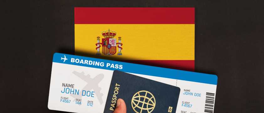 Pasaporte y tarjeta de embarque frente a bandera de España, viaje y requisitos migratorios.