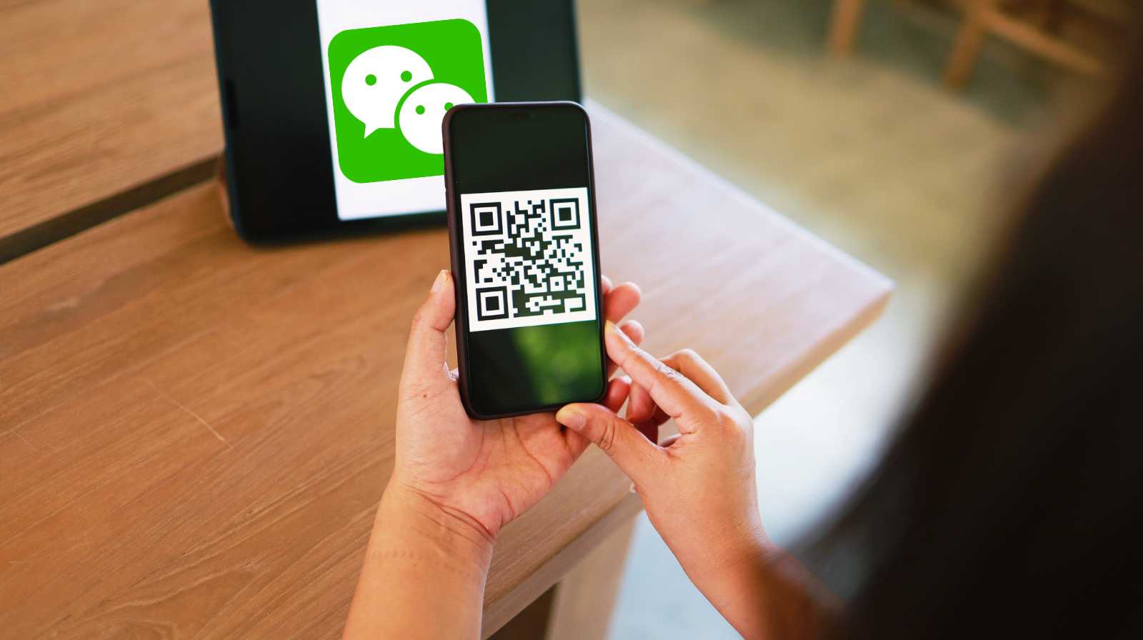 Une personne scannant un code QR avec WeChat depuis son téléphone, face à un autre appareil affichant le logo de l'application.