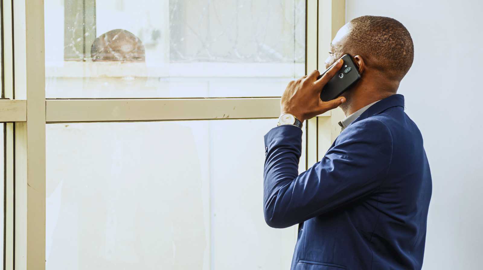 Man in a blue suit talking on a mobile phone while looking out of a lit window