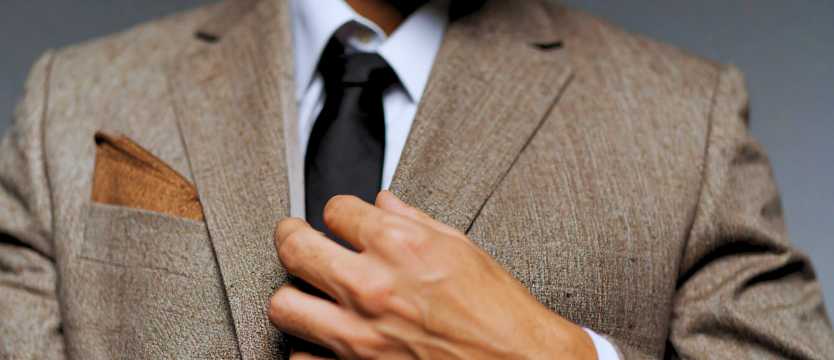 Primer plano de hombre ajustando la solapa de su traje con pañuelo en el bolsillo
