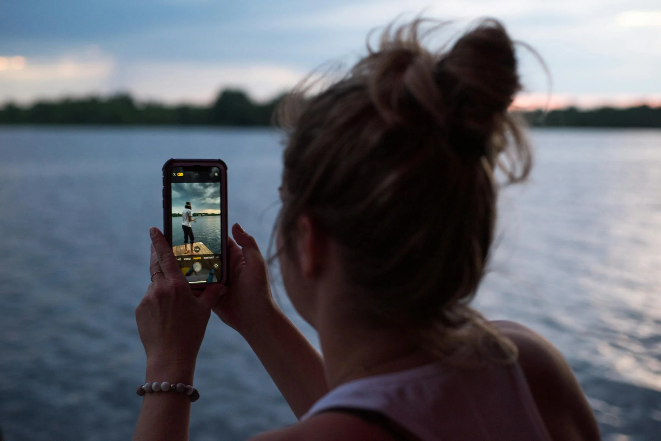 A girl holding a phone recording her friend by the beach