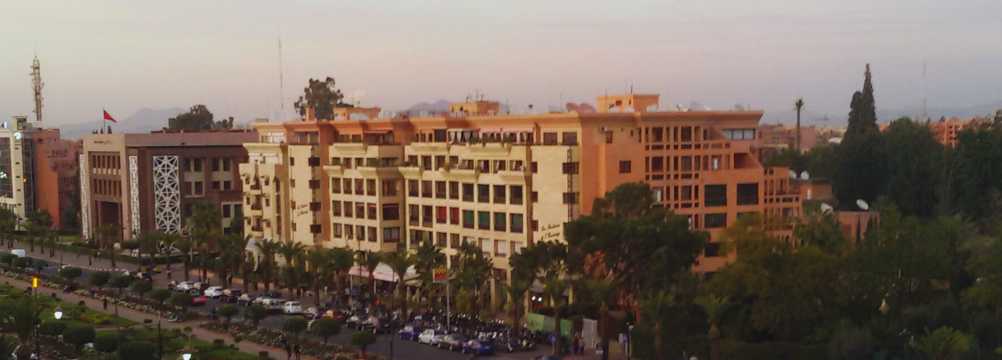 Vista urbana de Marrakech con edificios ocres, palmeras y tráfico al atardecer