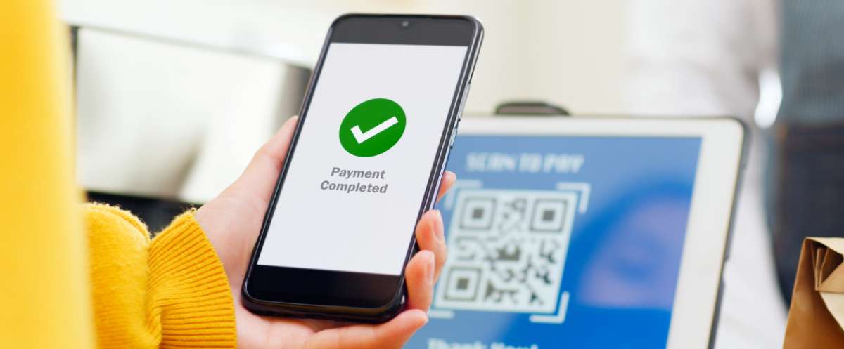 Personne tenant un téléphone portable affichant la confirmation « Payment Completed » après avoir scanné un code QR