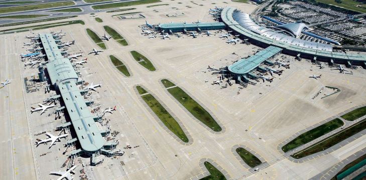 Modern airport terminal interior with glass ceilings, elevated walkways, and passenger facilities.