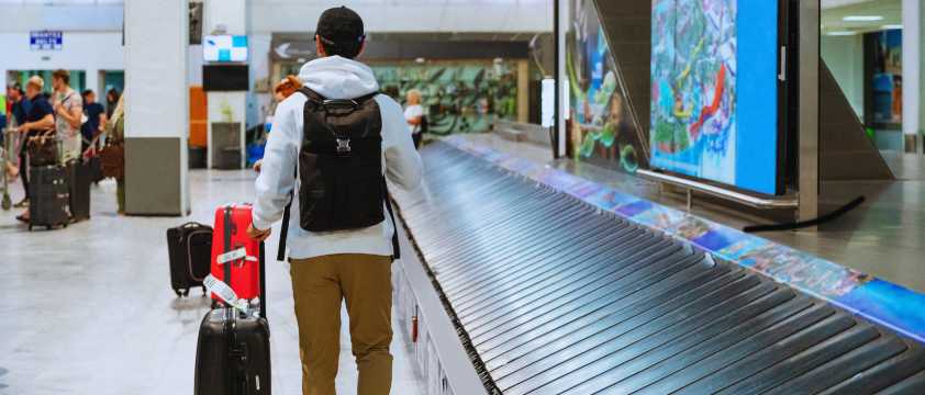 Viajero en aeropuerto esperando equipaje en cinta transportadora, llegada internacional.