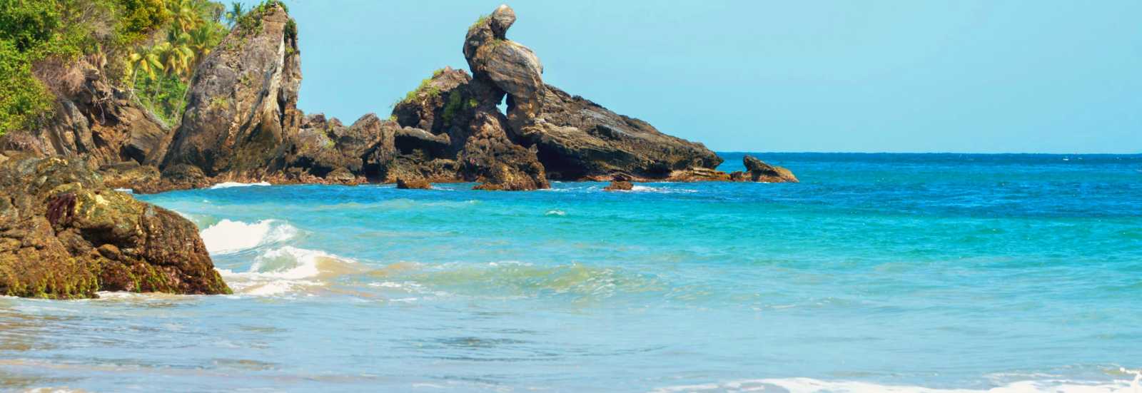 Playa tropical de aguas turquesa con formaciones rocosas escarpadas y vegetación exuberante junto al mar