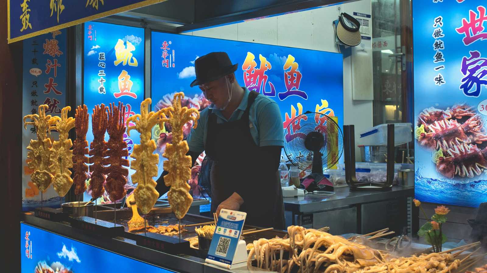Puesto de comida callejera en China con pinchos fritos y vendedor preparando snacks tradicionales