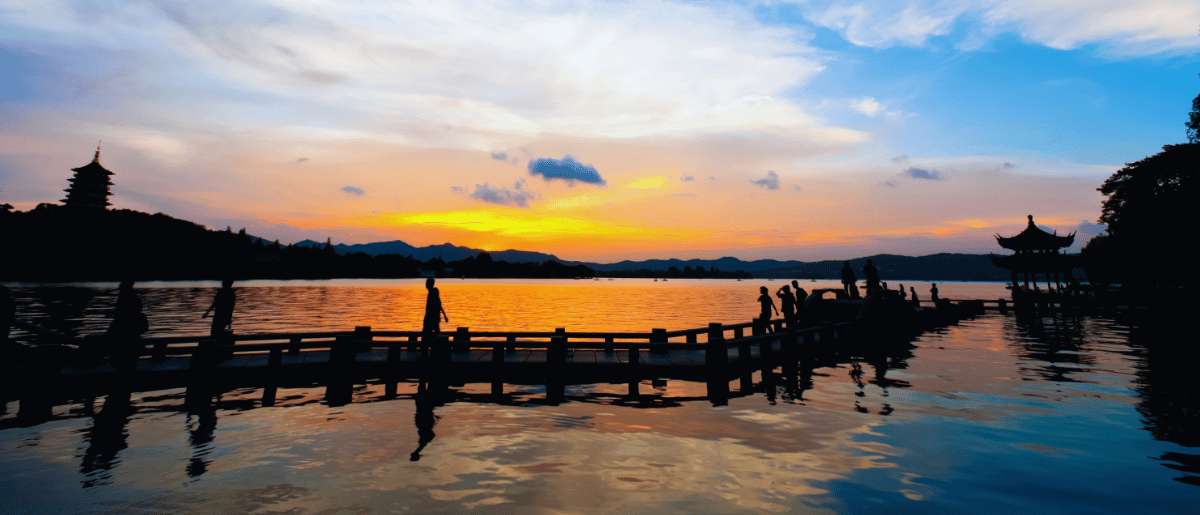 Coucher de soleil sur le lac de l'Ouest avec les silhouettes des visiteurs sur la passerelle et une pagode en arrière-plan
