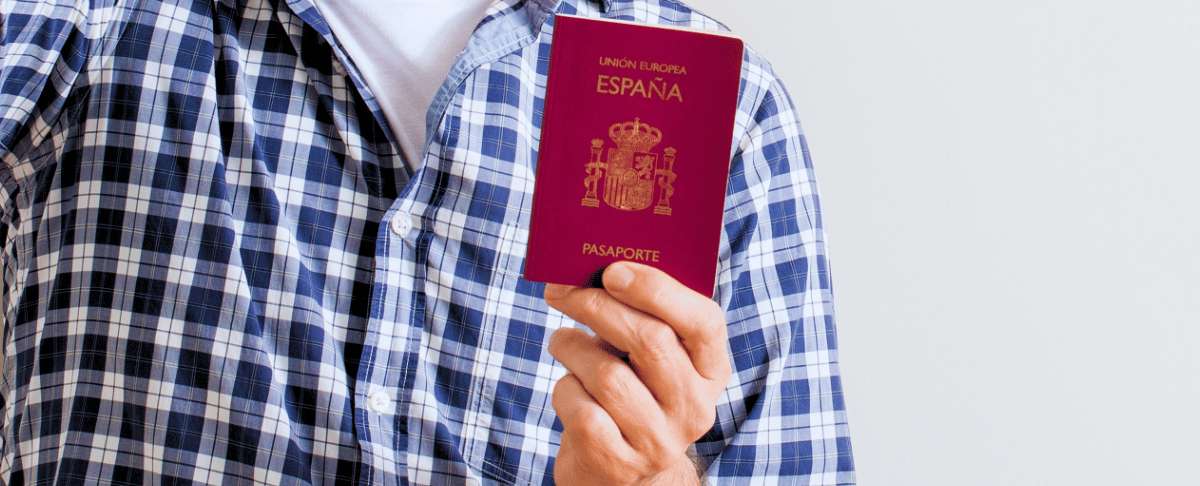 Persona sosteniendo pasaporte español en primer plano sobre fondo neutro