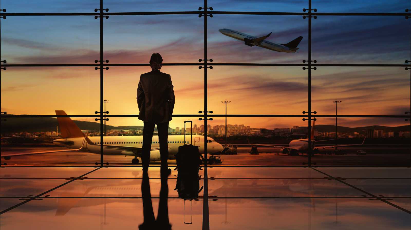 Viajero en un aeropuerto observando un avión despegar al atardecer