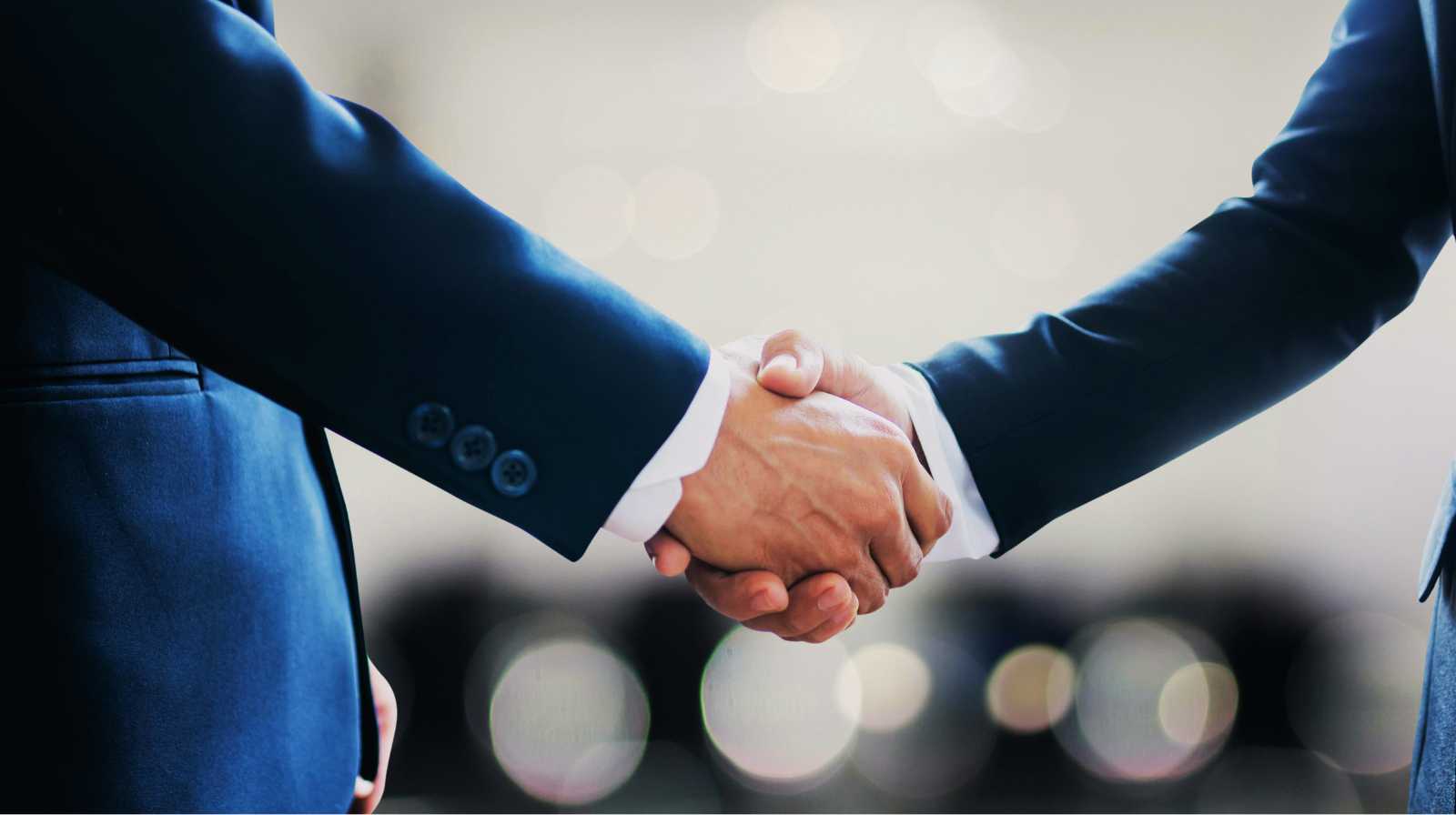 Two people in suits shaking hands in a professional setting, symbolising agreement or collaboration