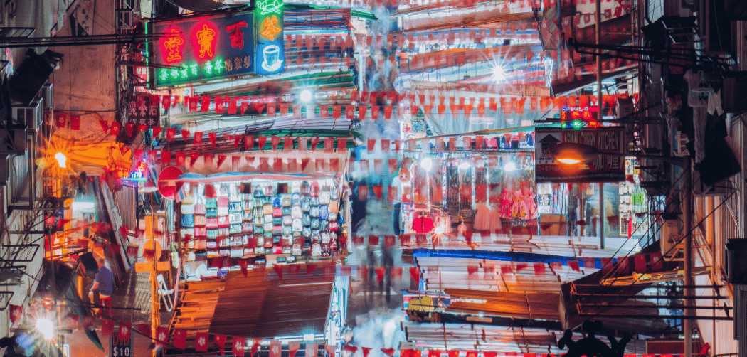 Un marché de rue à Hong Kong, baigné dans la lueur des néons et une atmosphère nocturne vibrante.