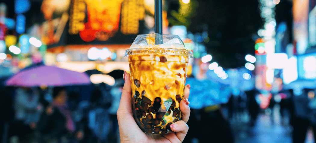 Un bubble tea taïwanais aux perles de tapioca, tenu dans une rue lumineuse de Taipei.