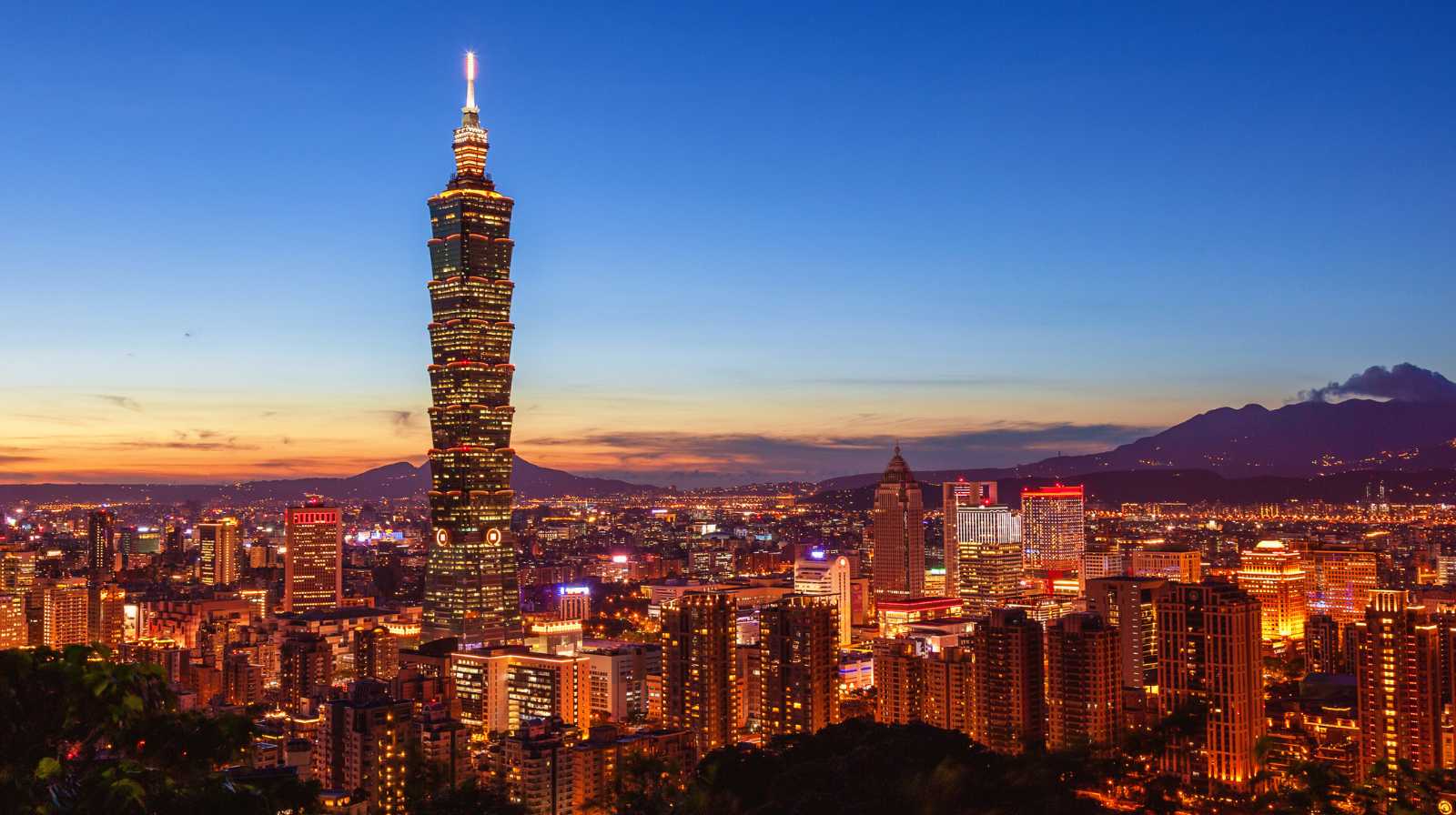 Panorámica del Taipei 101 iluminado al anochecer con la ciudad de Taipéi extendiéndose bajo un cielo azul profundo