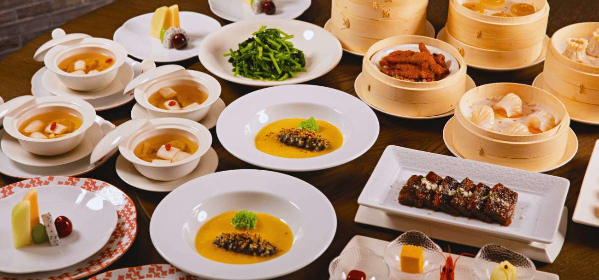 Mesa con variedad de platos de alta cocina china, incluyendo sopas, dim sum al vapor en cestas de bambú y costillas glaseadas