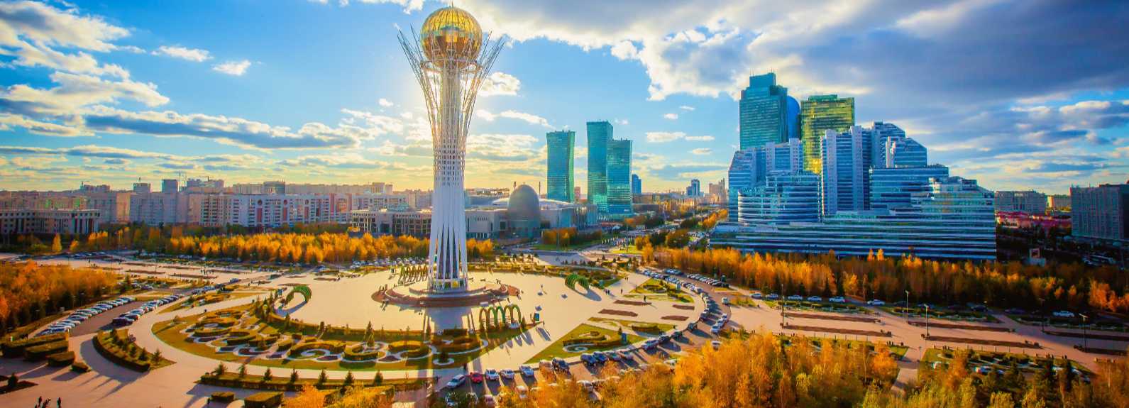 Vista panorámica de Astaná con la torre Bayterek en el centro y edificios modernos rodeados de parques urbanos