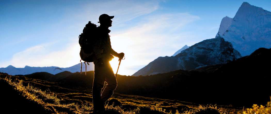 Wanderer mit Rucksack und Wanderstöcken genießt eine Trekkingtour zwischen den Bergen bei Sonnenaufgang