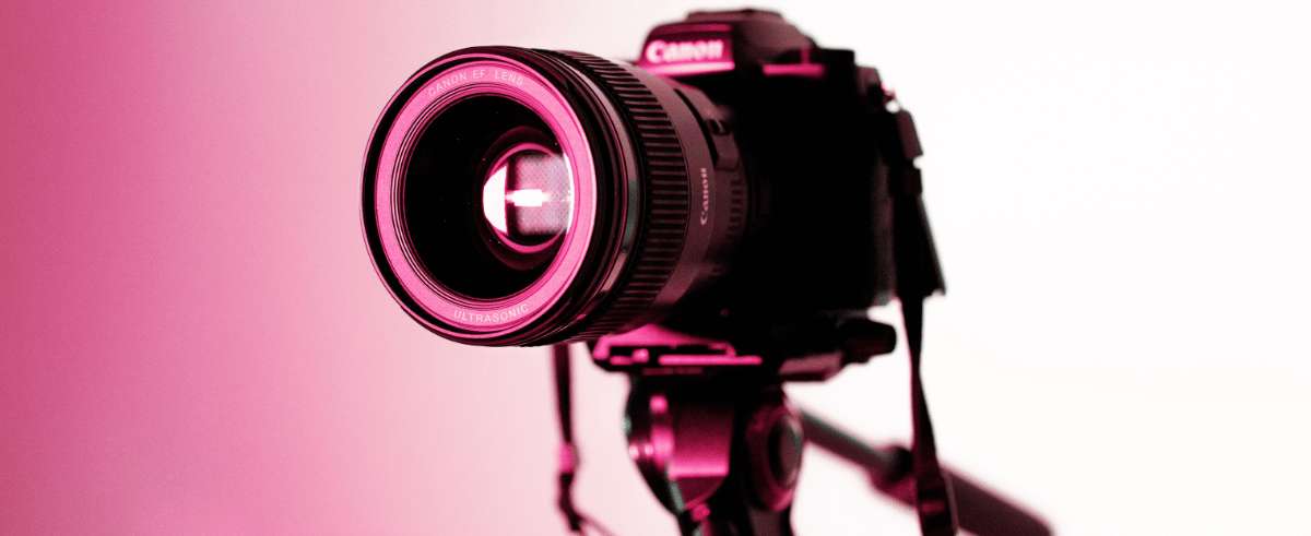 Canon DSLR camera with lens illuminated in pink tones against a gradient background