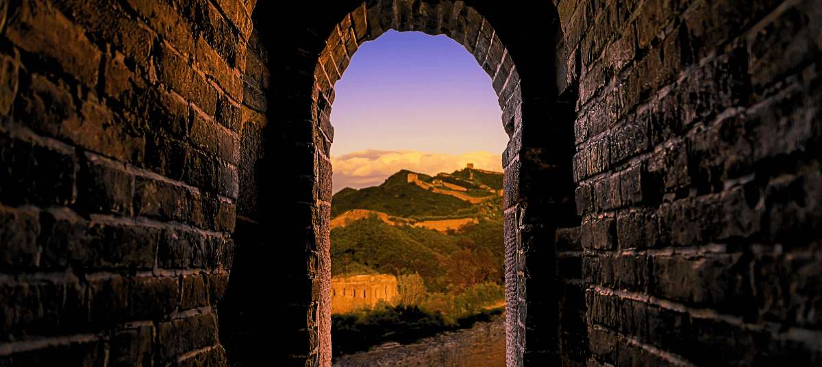 Vista de la Gran Muralla China a través de un arco de piedra al atardecer