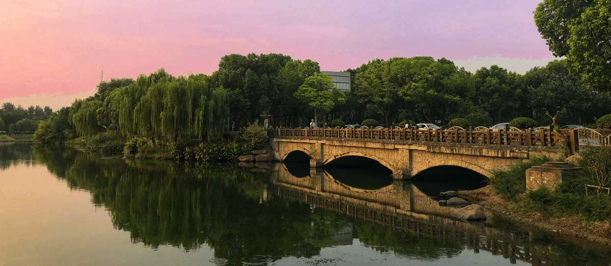 Puente de piedra sobre río tranquilo rodeado de árboles y reflejos en el agua en Suzhou