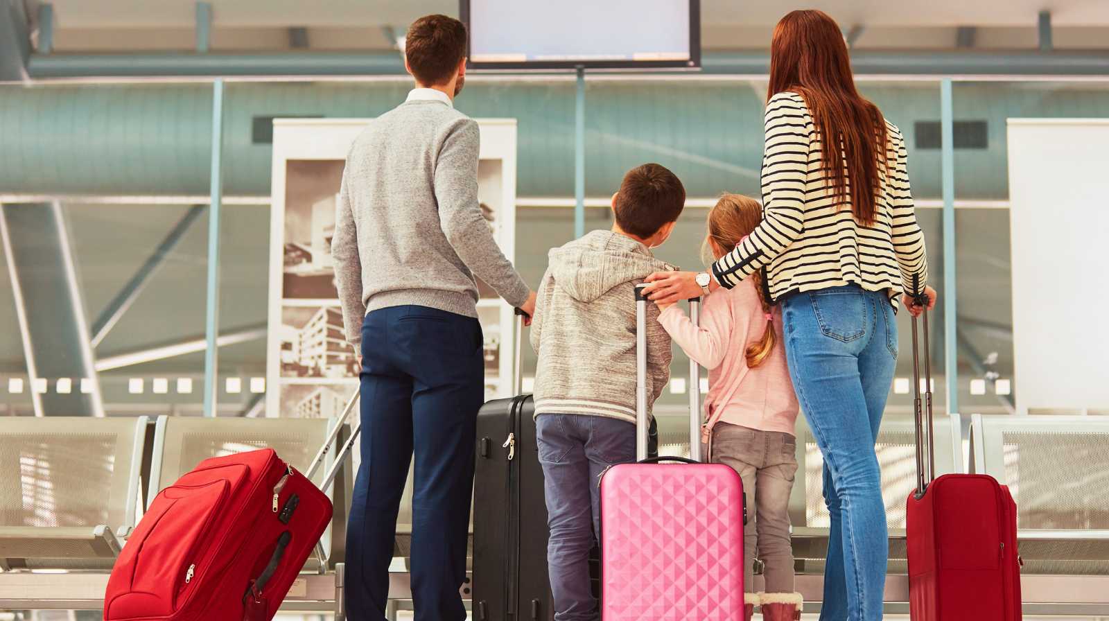 Family with two children looking at the flight information board at an airport with their suitcases