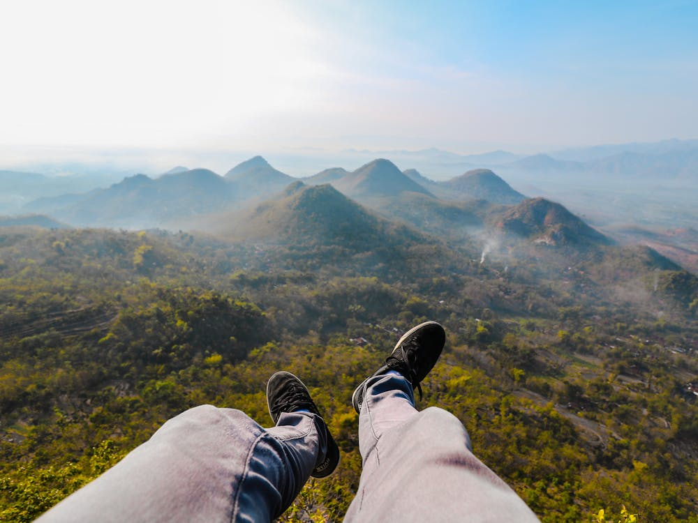 A pair of legs in shot, cameraman is sitting on a ledge looking at the mountain views