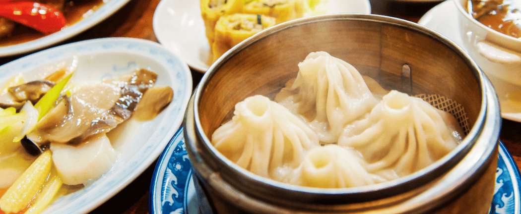 Xiaolongbao (dumplings al vapor rellenos de caldo) servidos en una vaporera de bambú junto a otros platos chinos
