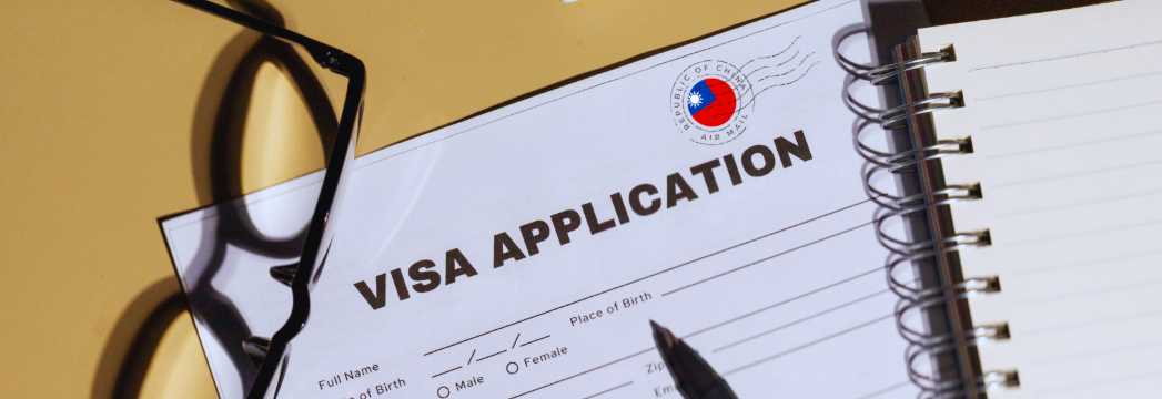 Formulario de solicitud de visa con bolígrafo y gafas sobre escritorio, trámite de visado internacional.