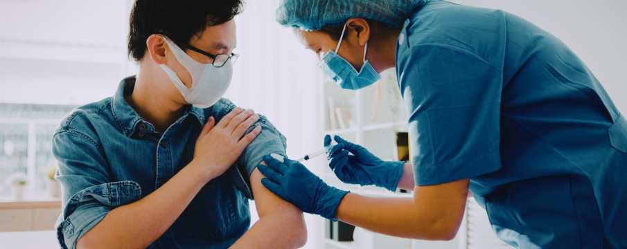 Medizinische Fachkraft verabreicht einem Reisenden mit Maske eine Impfung – eine wichtige Gesundheitsvoraussetzung für internationale Reisen.