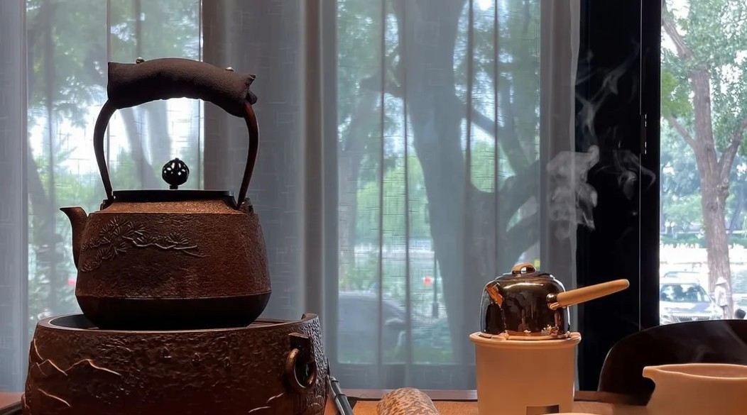 Chinese tea ceremony setup with a cast-iron kettle, teapot, and tasting cup