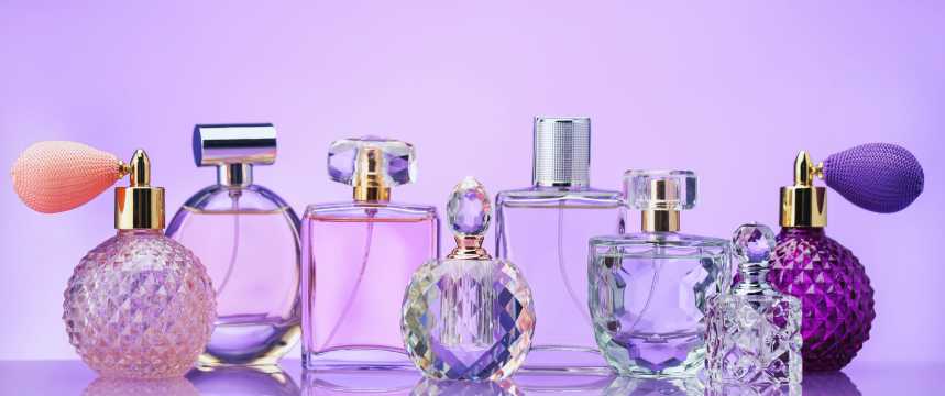 Una collezione di boccette di profumo in cristallo su uno sfondo lilla con un'illuminazione soffusa