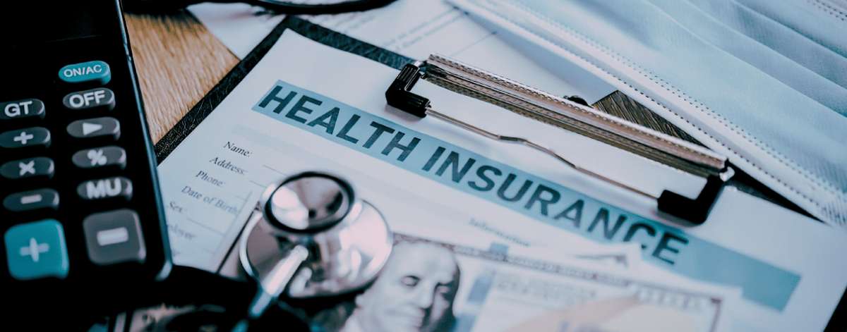 Document d'assurance santé accompagné d'une calculatrice, d'un masque et d'un stéthoscope sur un bureau.