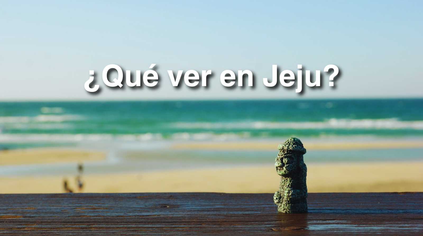 Pequeña estatua Dol Hareubang sobre una baranda con la playa y el mar de Jeju al fondo junto al texto “¿Qué ver en Jeju?”