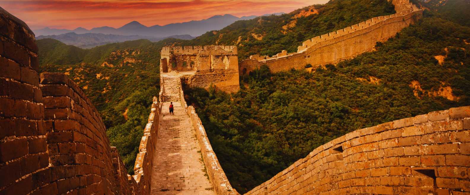 Tramo de la Gran Muralla China al atardecer, rodeado de colinas verdes y murallas históricas