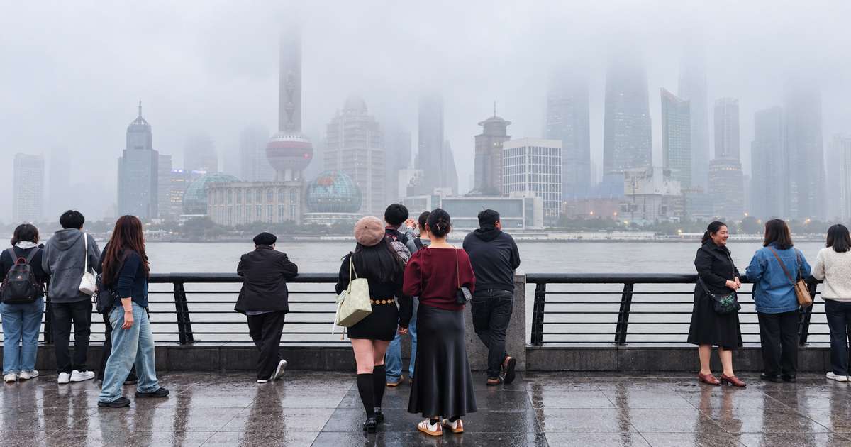 Visitantes no Bund diante do skyline de Pudong encoberto por névoa