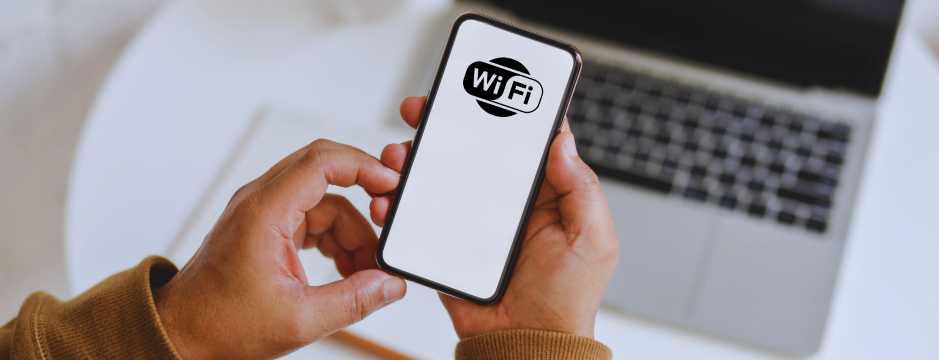 Persona sosteniendo smartphone con símbolo WiFi, conexión a internet y uso de datos durante viajes internacionales.