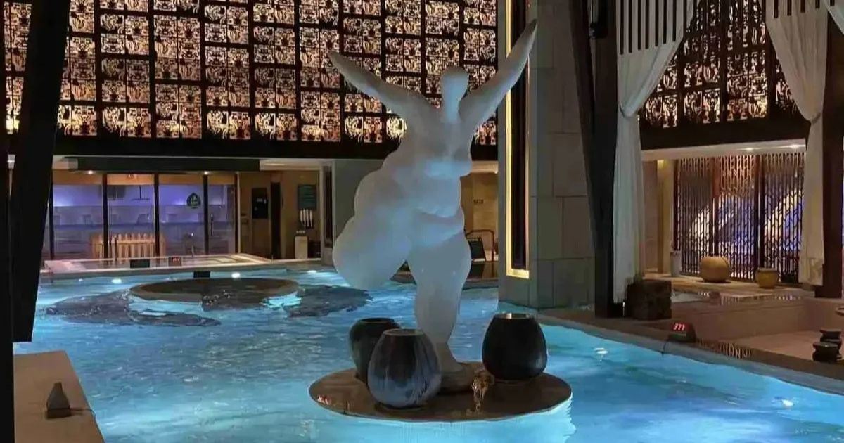 Beleuchteter Innenpool des Qingshuiwan Letanghui mit zentraler Skulptur und Ruhebereichen. 