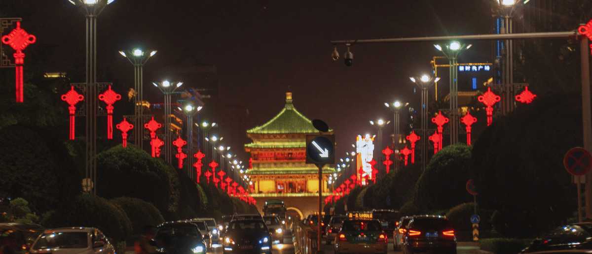 Avenida iluminada de Xi’an de noche con faroles rojos y la Torre del Tambor al fondo, tráfico urbano en China