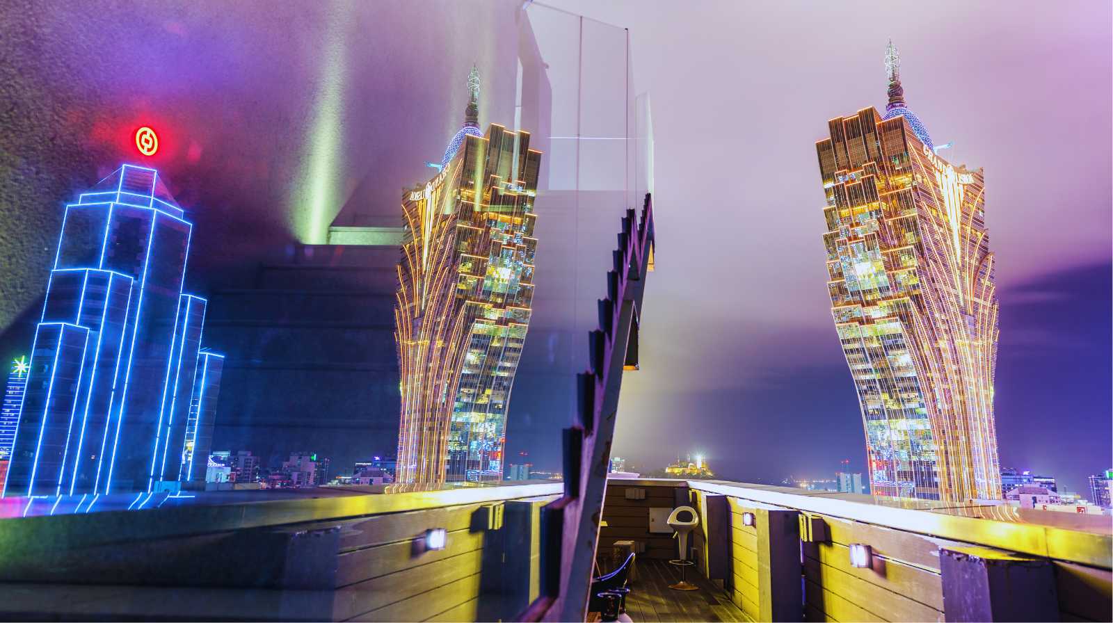 Night-time view of the Grand Lisboa in Macau reflected in a pane of glass, with neon lights and a terrace in the foreground