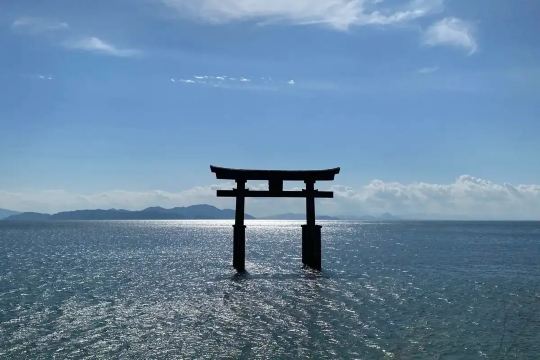 Torii gate standing in the sea with mountains on the horizon