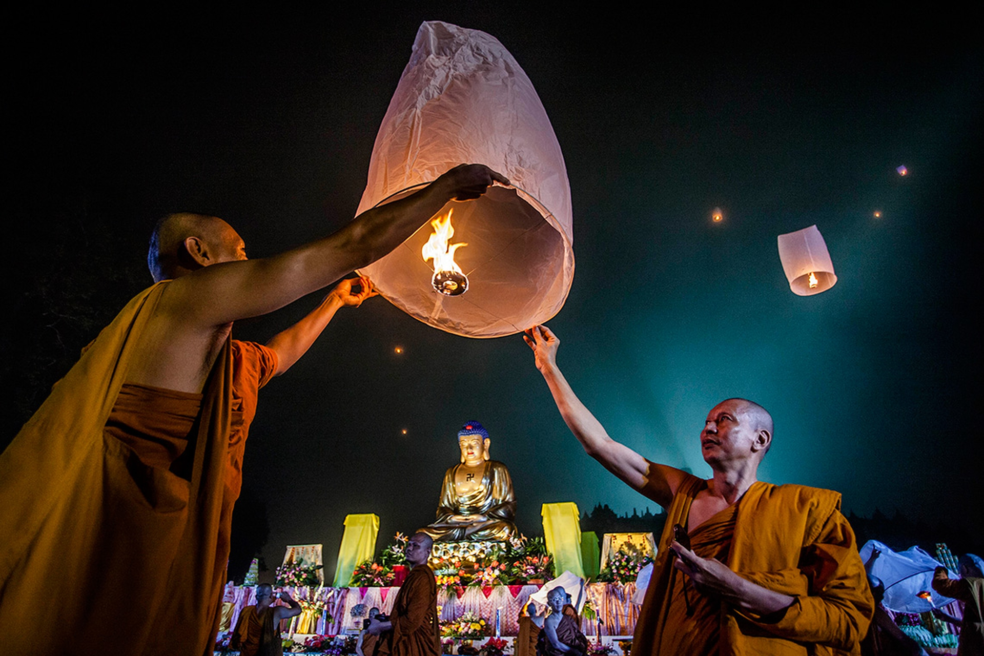 a pair of monks letting a flying candle go in front of a buddha statue