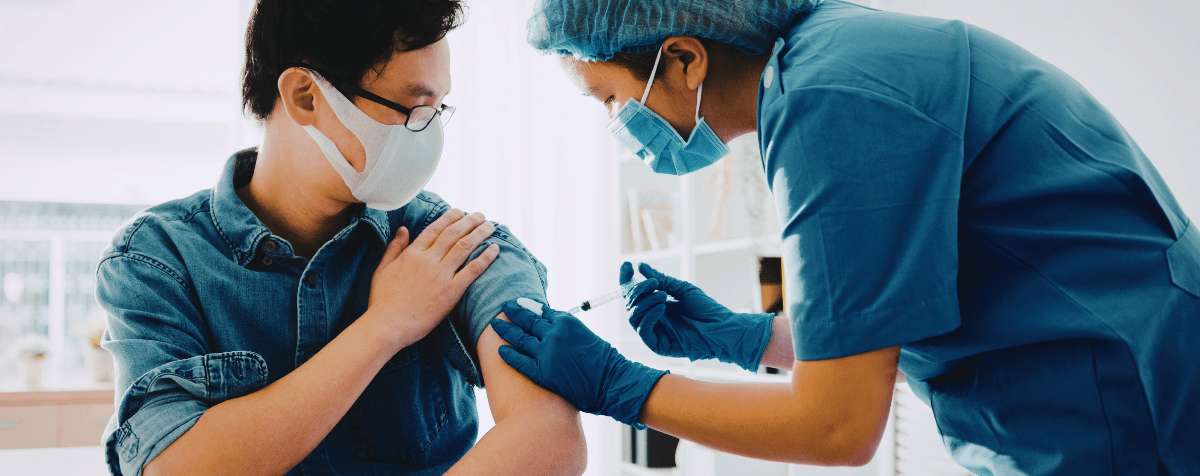 Person receiving a vaccine in their arm from a healthcare professional wearing a mask in a clinical setting
