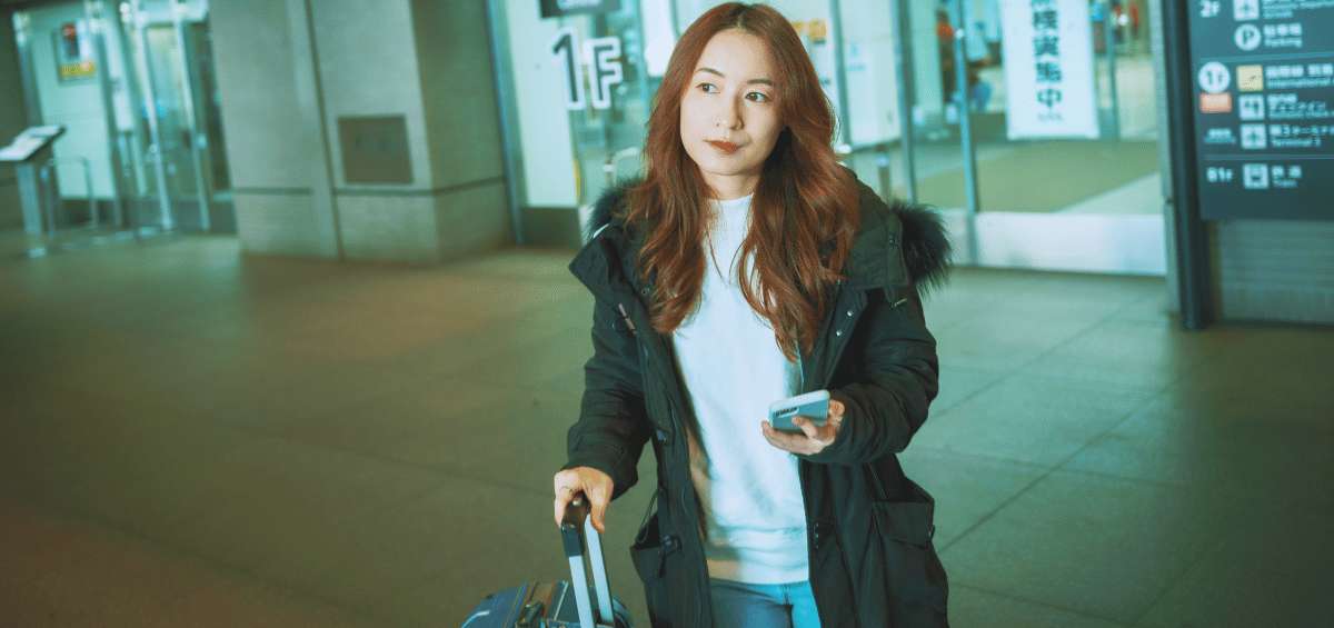 Female traveller with a suitcase using her mobile phone at a modern airport or station