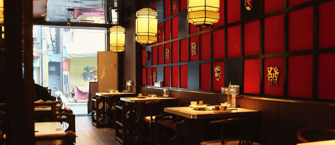Intérieur d'un restaurant chinois traditionnel avec des lanternes suspendues, des tables en bois et une décoration rouge agrémentée de panneaux et de symboles asiatiques